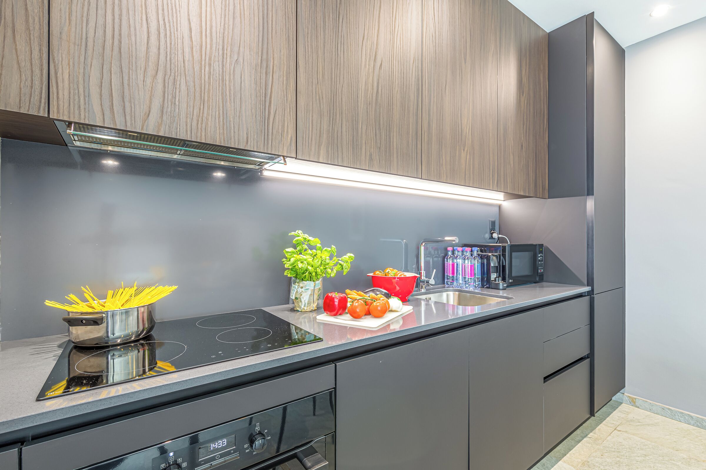 A modern kitchen with dark cabinetry, a stainless steel countertop, and an induction cooktop.