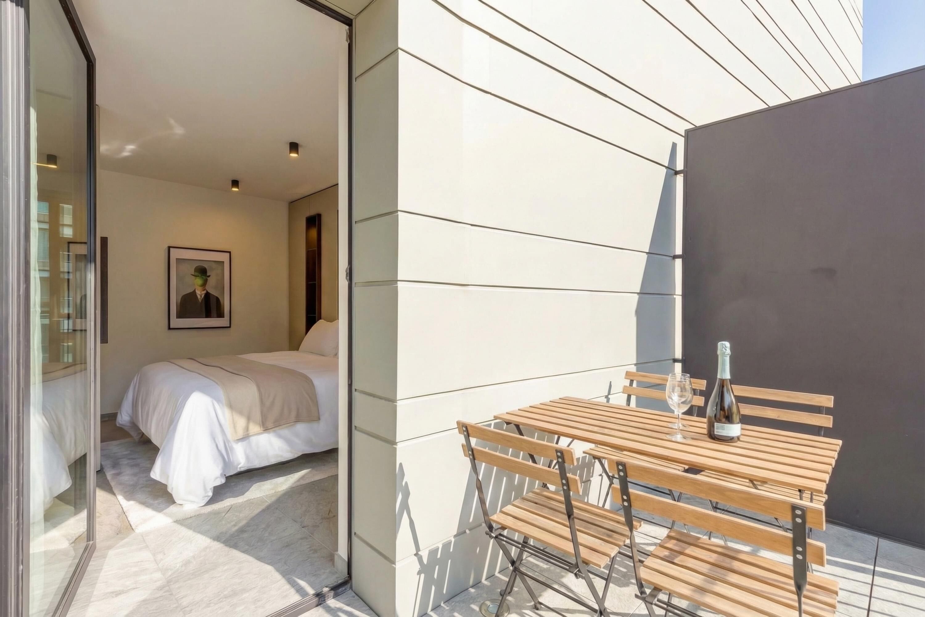 A modern room with a bed, a wooden table with a bottle and glass, and a framed picture on the wall.