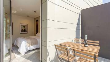 A modern room with a bed, a wooden table with a bottle and glass, and a framed picture on the wall.