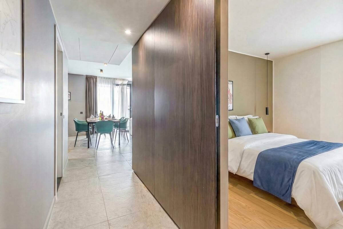 A modern hotel room with a bed, a desk, and a dining area with chairs.