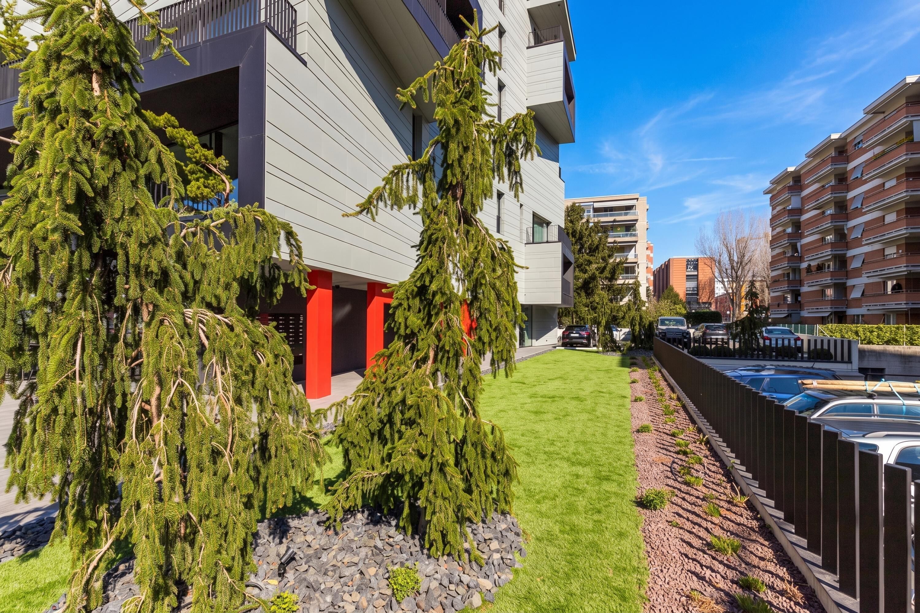 A modern building with a red pillar, a well-maintained lawn, and a parking area.