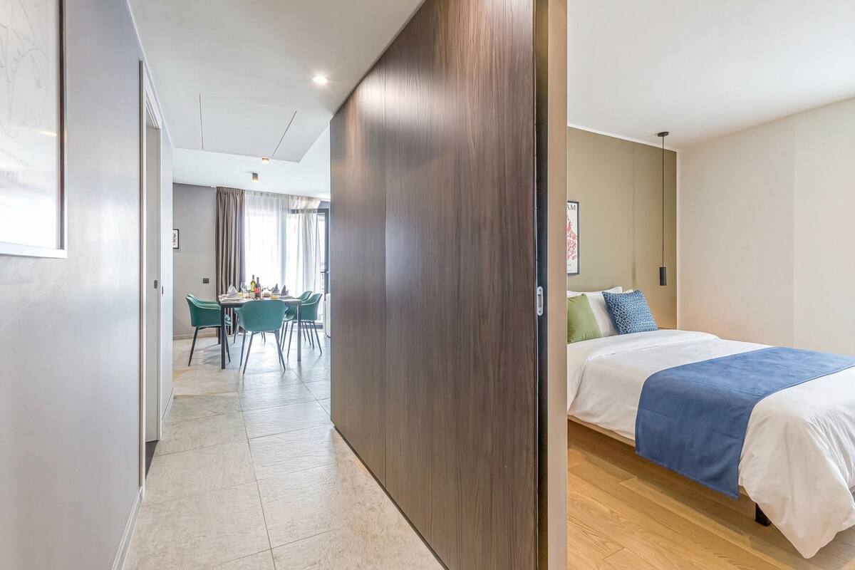 A hotel room with a bed, a dining area with chairs, and a view of the outdoors.