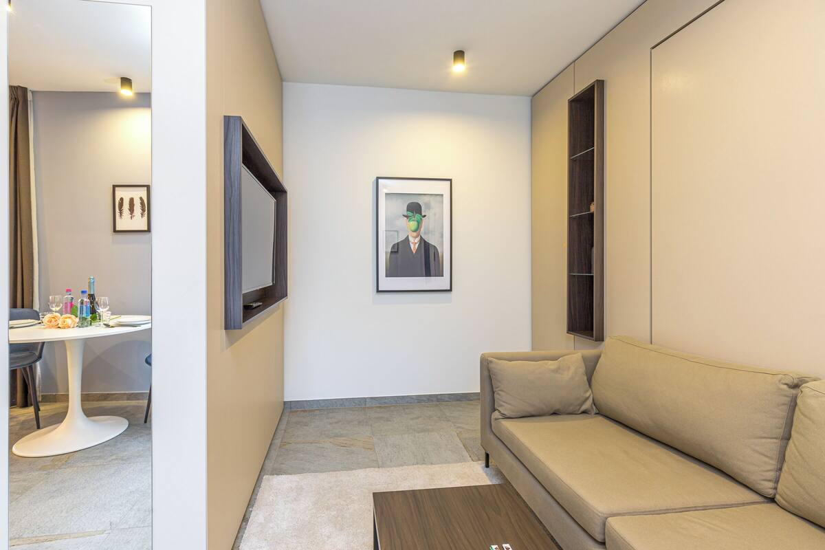 A modern living room with a sofa, a coffee table, a dining table with chairs, and artwork on the walls.
