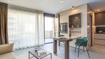 A modern living room with a sofa, coffee table, and a dining area with chairs. There is a sliding door leading to a balcony.