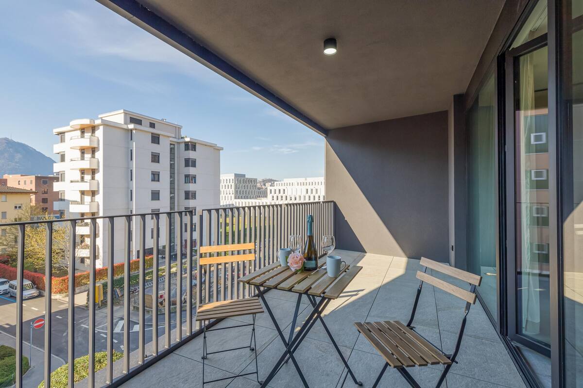 A balcony with a table and chairs, a bottle of champagne, and a view of buildings and a street.