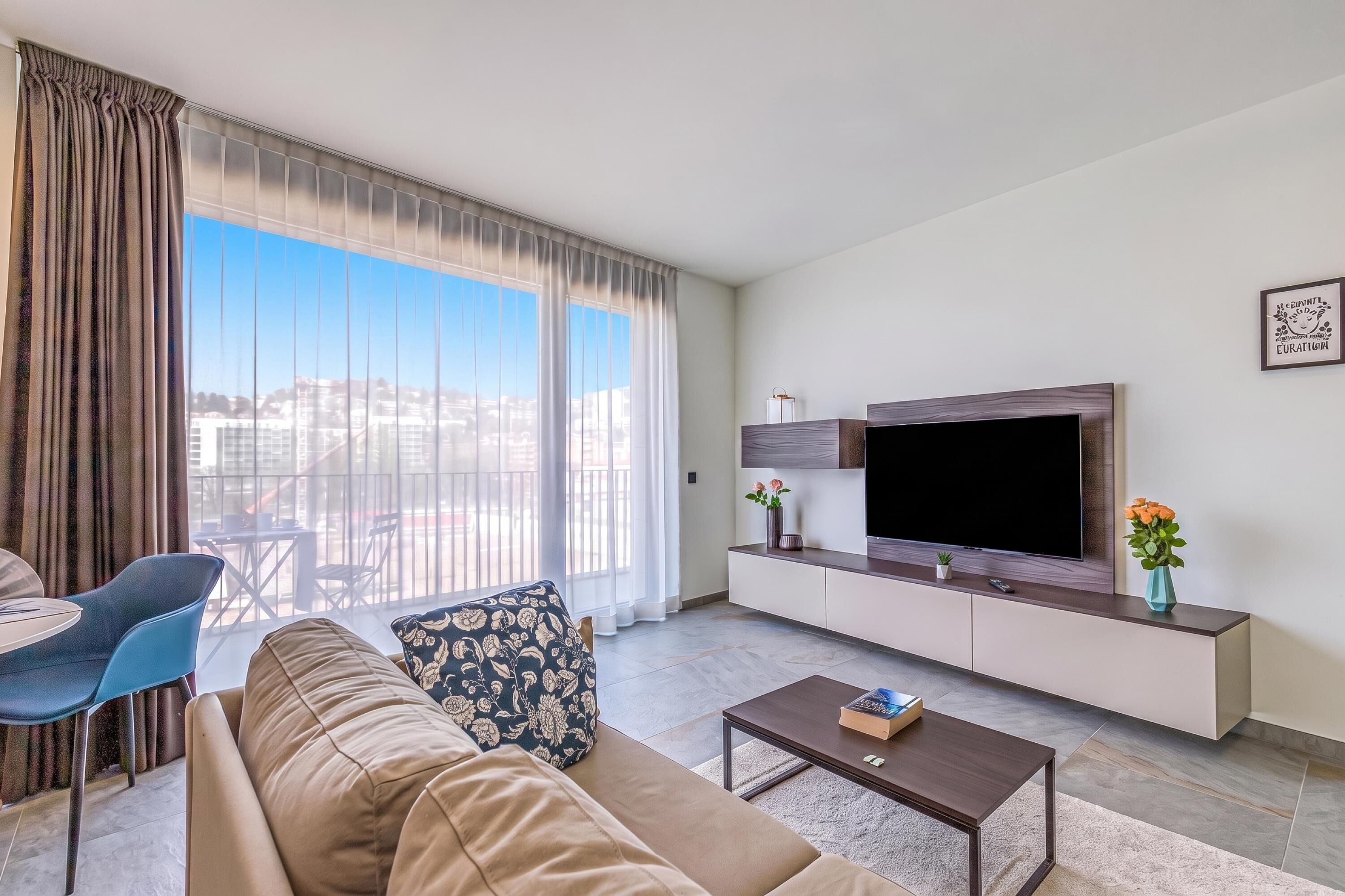 A modern living room with a sofa, coffee table, TV, and a view of the city through large windows.