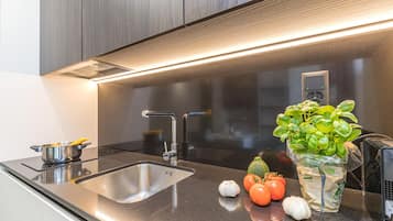A modern kitchen with a stainless steel sink, a built-in stove, and a potted basil plant.