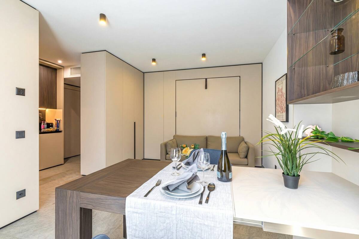 A modern dining area with a table set for two, a sofa, and a potted plant.