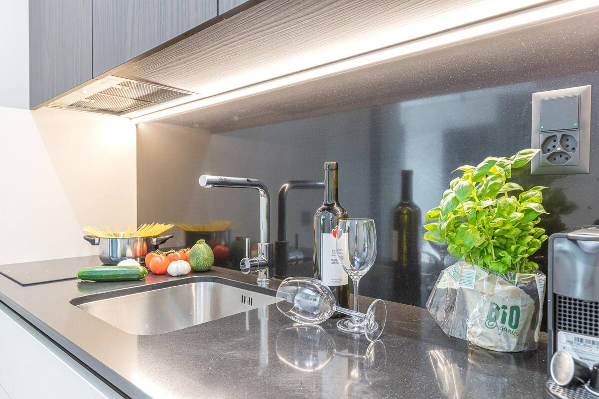 A modern kitchen with a stainless steel sink, a faucet, a wine glass, and a potted plant.