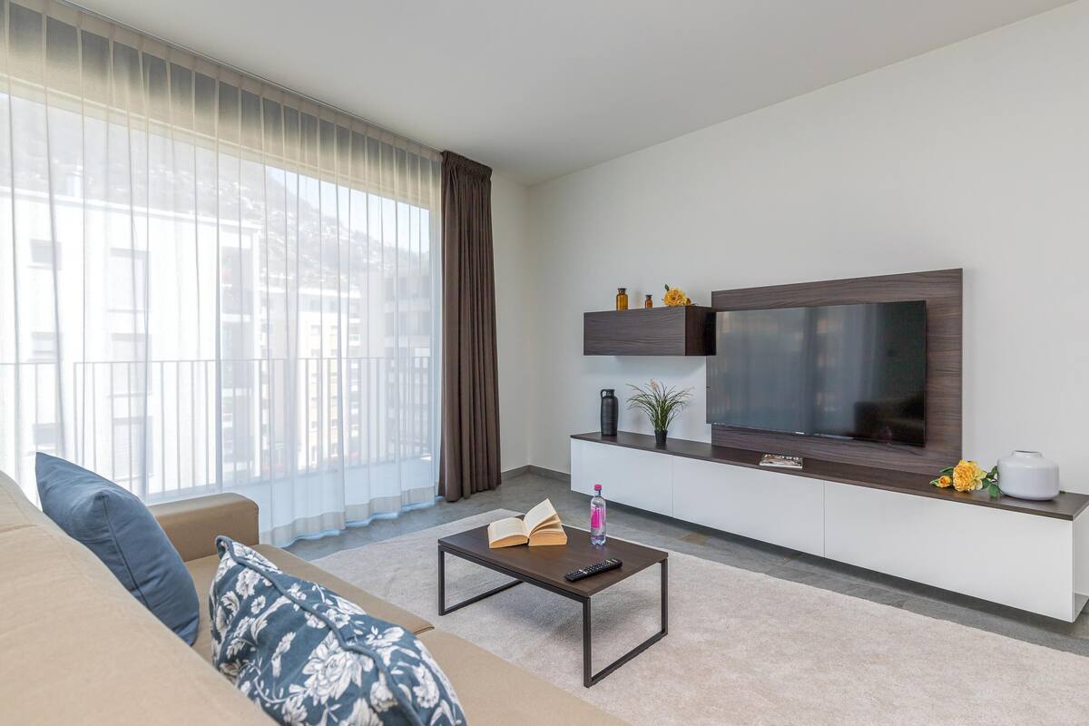 A modern living room with a sofa, coffee table, and a flat-screen TV mounted on the wall.