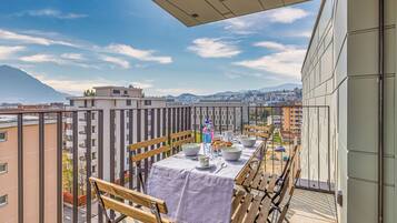 A balcony with a table set for dining, overlooking a cityscape and mountains.