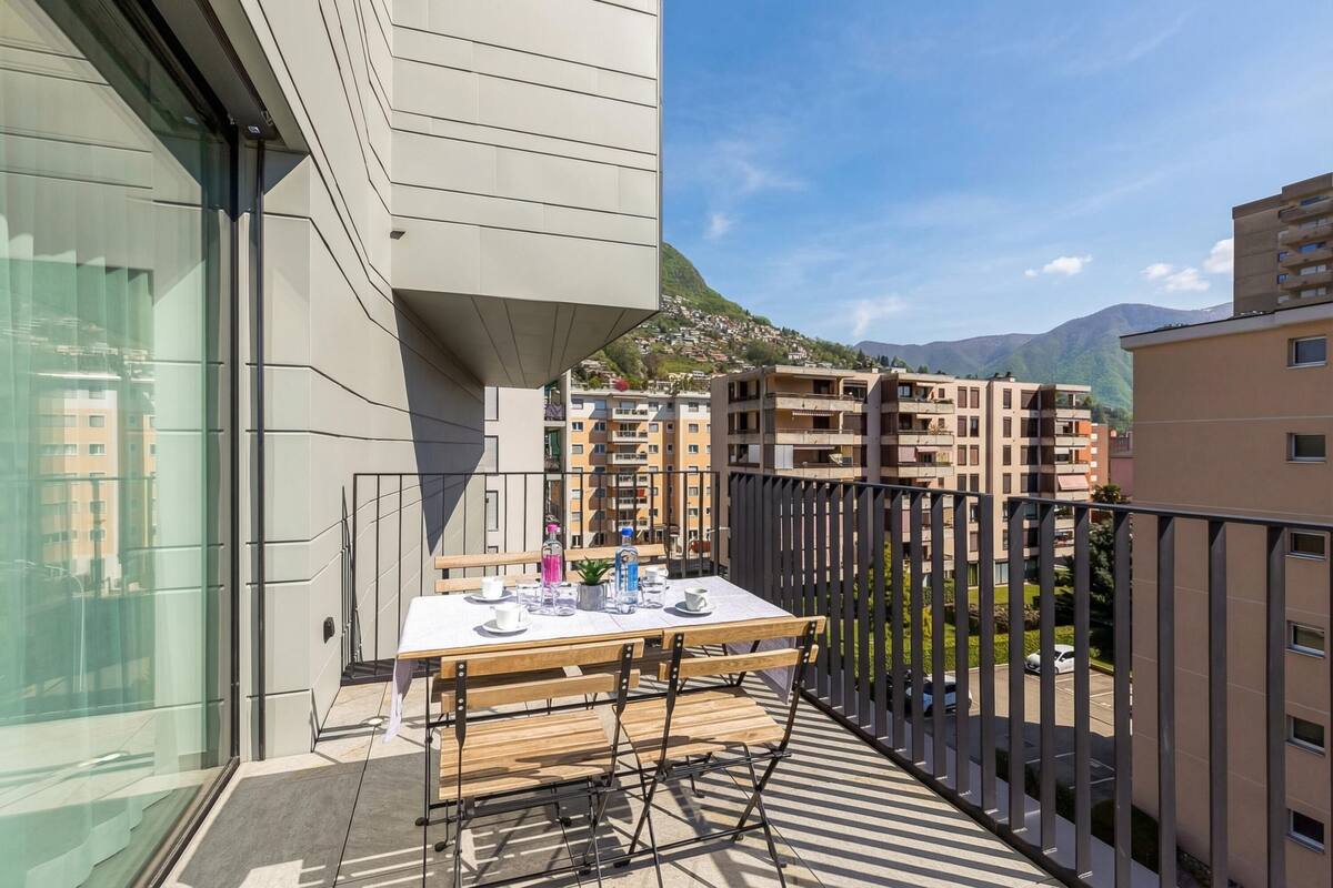 A balcony with a table set for dining, a view of residential buildings, and a mountain in the background.