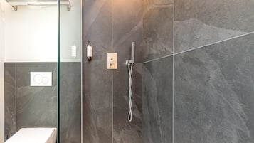 Un bagno moderno con cabina doccia in vetro, un water e un dispenser di sapone a parete.