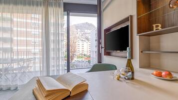 Habitación de hotel con un ventanal grande, una mesa de comedor con un libro abierto, una botella y un plato con fruta.