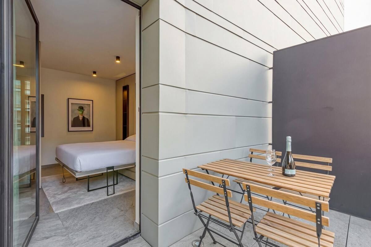 A modern room with a bed, a table with chairs, and a bottle of wine.