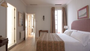Habitación de hotel con cama, mesita de noche, lámpara, un cuadro en la pared y ventana con cortinas.