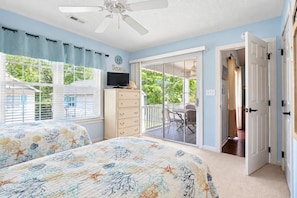 A bedroom with a bed, a dresser, a television, and a sliding glass door leading to a balcony.