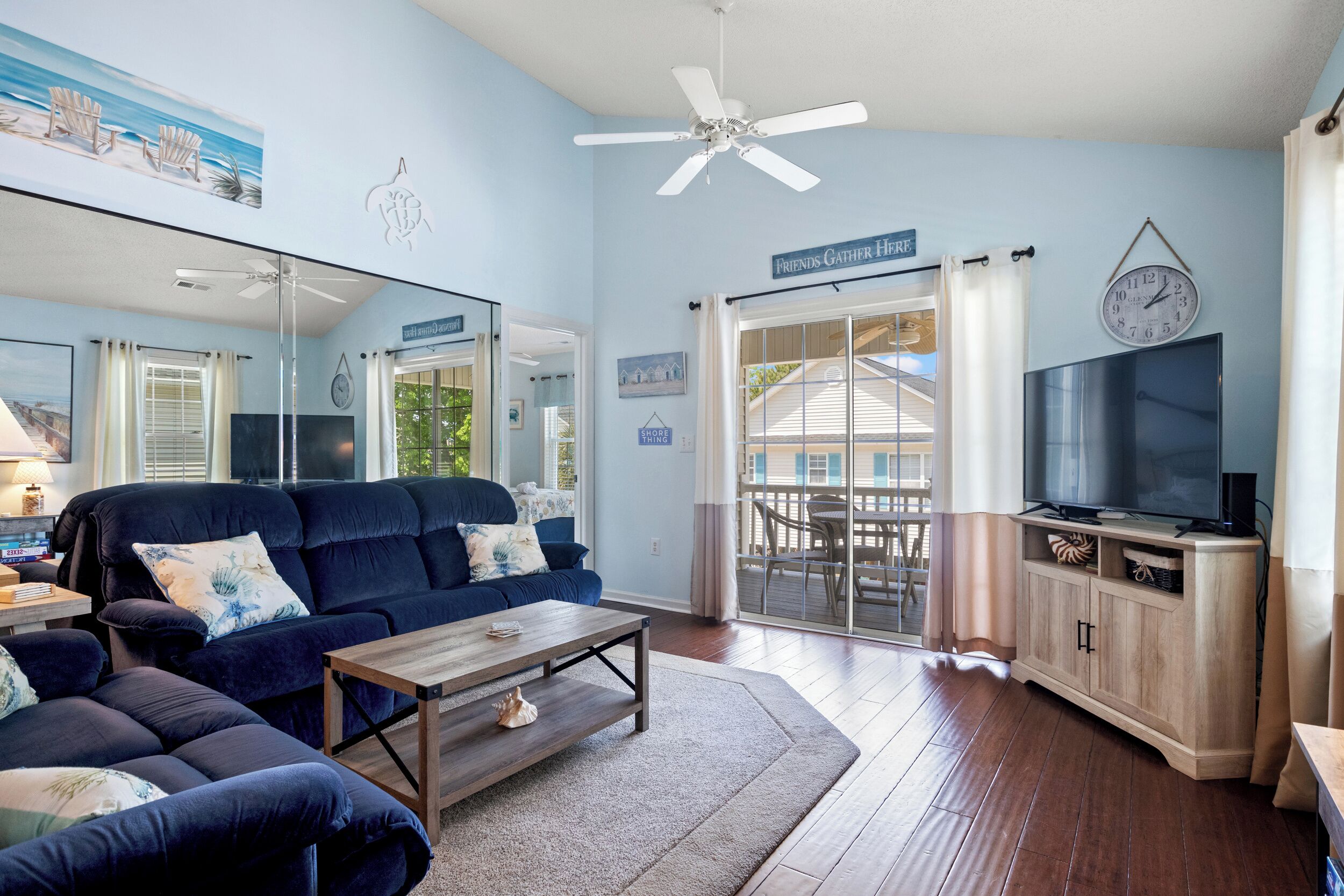 Un salon avec un canapé bleu, une table basse, un téléviseur et un ventilateur de plafond.