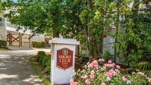 Schild des Shore Club East, umgeben von üppigem Grün und rosafarbenen Rosen.
