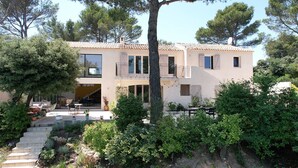Una casa de dos pisos con un balcón, una escalera que lleva al nivel superior y un jardín con mobiliario exterior.