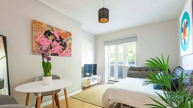 Une chambre moderne avec un lit, une télévision, une table à manger avec des chaises et une grande fenêtre.