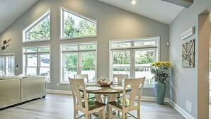 A spacious room with large windows, a dining table with chairs, a sofa, and a large vase with flowers.
