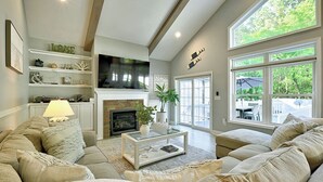 A cozy living room with a fireplace, comfortable seating, and a large window offering a view of the outdoors.