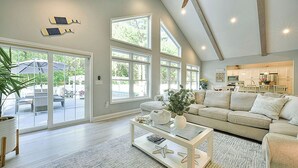 A spacious living room with a high ceiling, large windows, and a ceiling fan.