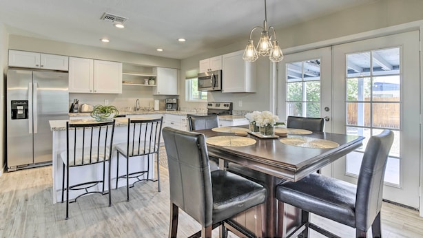 Una cocina moderna con armarios blancos, electrodomésticos de acero inoxidable y una zona de comedor con mesa de madera y sillas de cuero.