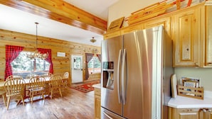 Interior de una cabaña con un refrigerador de acero inoxidable grande, una mesa de comedor de madera y techo de madera.