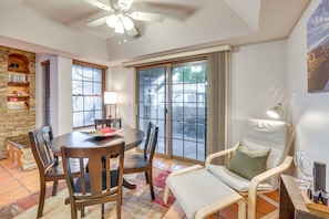 Relax in this open-plan living space with a dining area and seating area, featuring a ceiling fan and large window with a view of the outdoors.