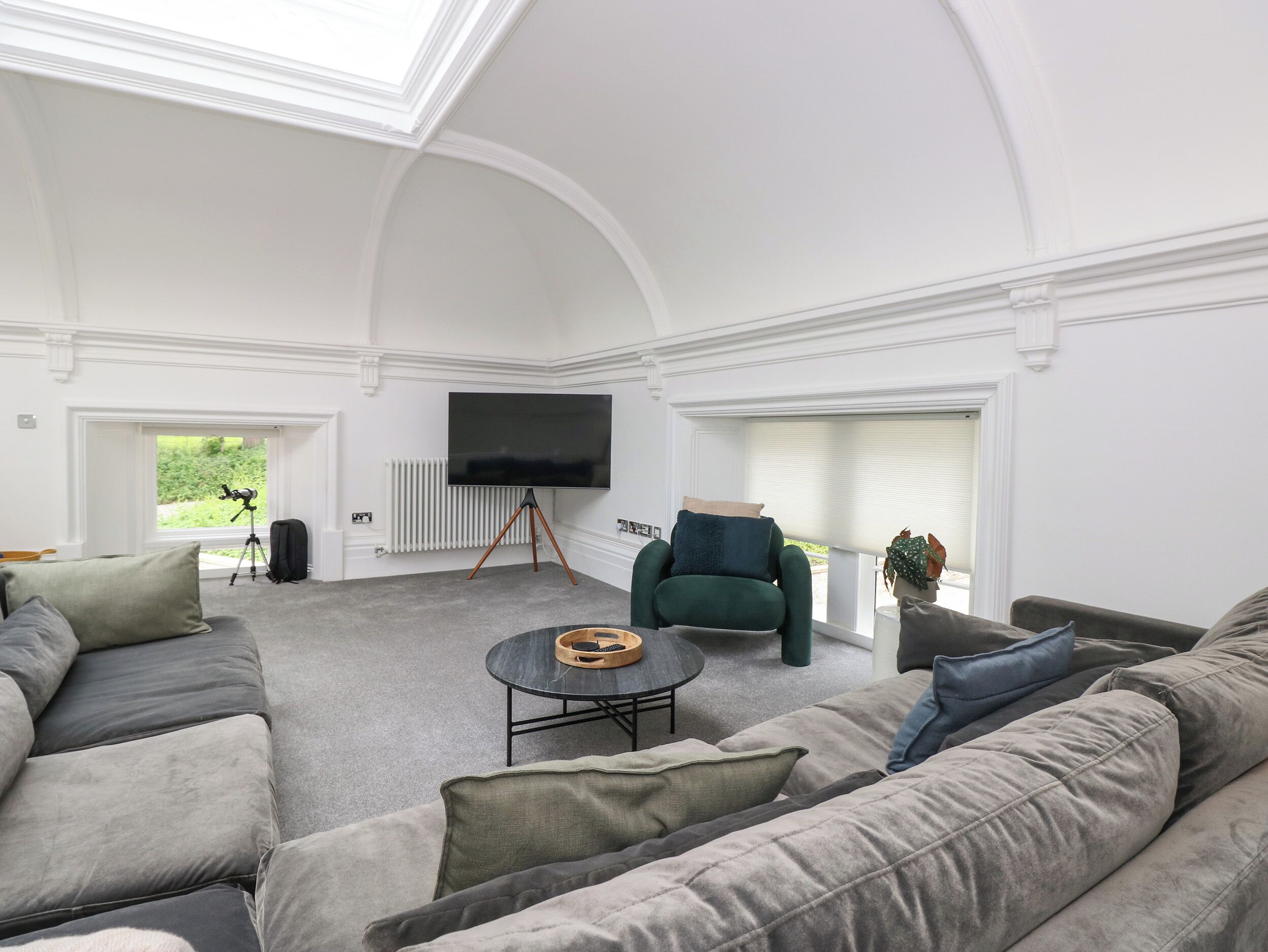 Ein geräumiges Wohnzimmer mit einer großen Eckcouch, einem runden Couchtisch und einem flachbildfernseher an der Wand.