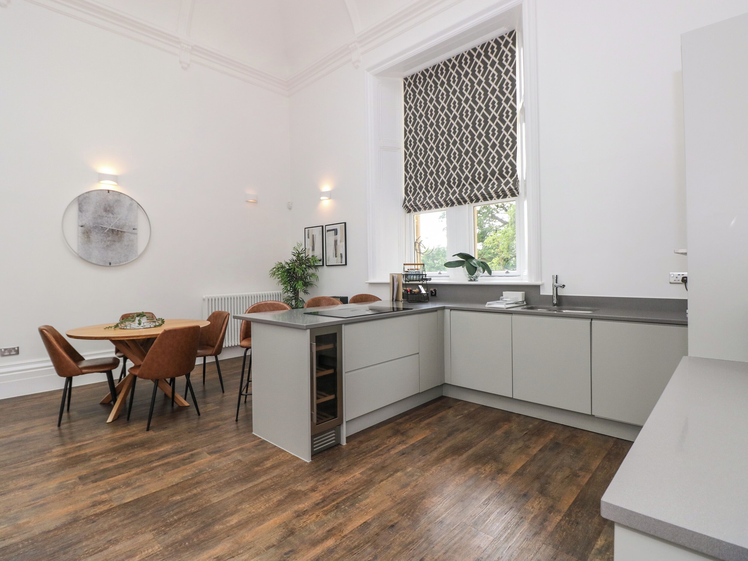 A modern kitchen with a built-in island, white cabinetry, and a window with patterned curtains.