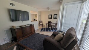 A living room with a TV, a sofa, a coffee table, a dining table with chairs, and a window with blinds. - DAPHNE -  MOBILE BAY CONDO - Great location  (Daphne)