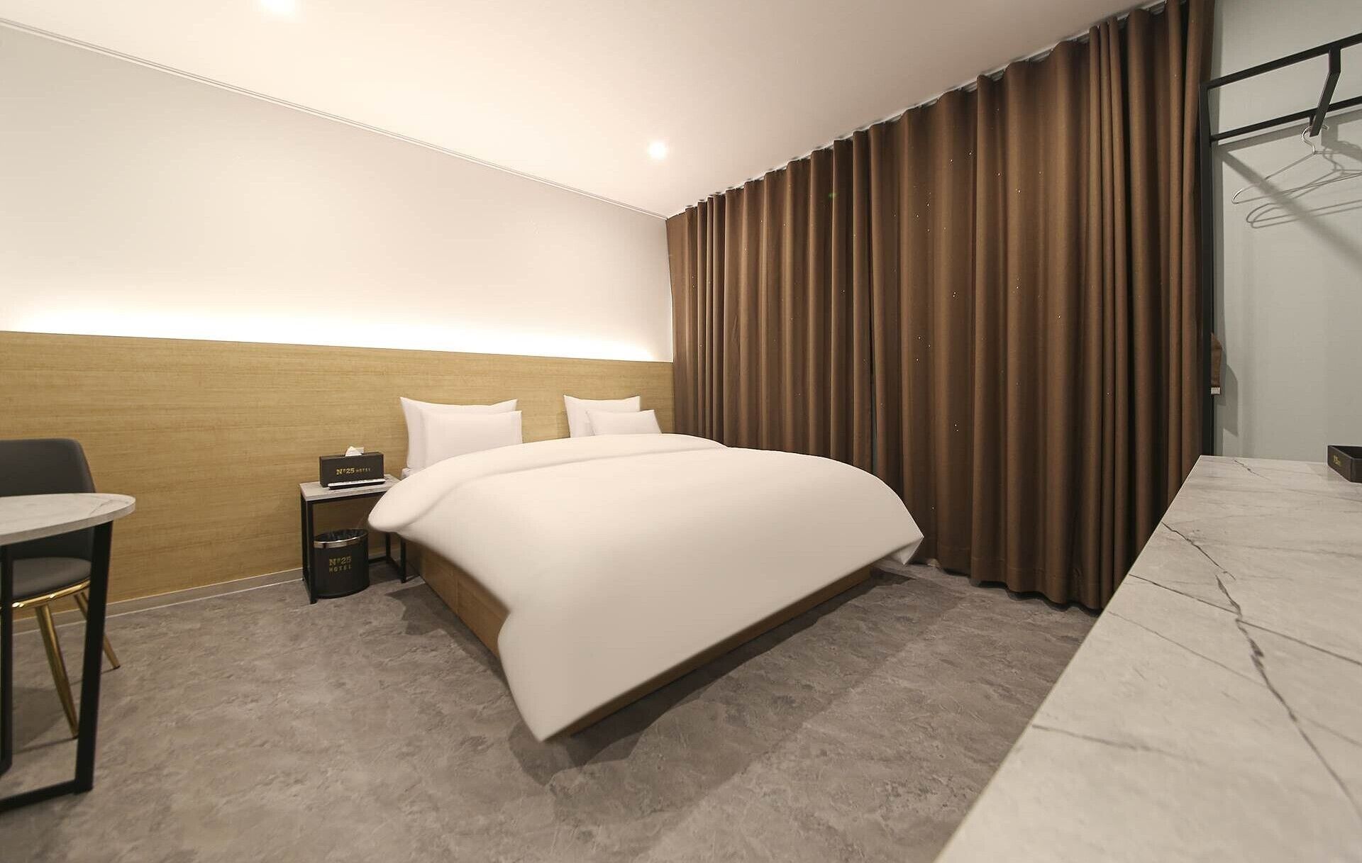 A hotel room with a large bed, a desk, a chair, and a wardrobe.