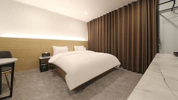 A hotel room with a large bed, a desk, a chair, and a wardrobe.