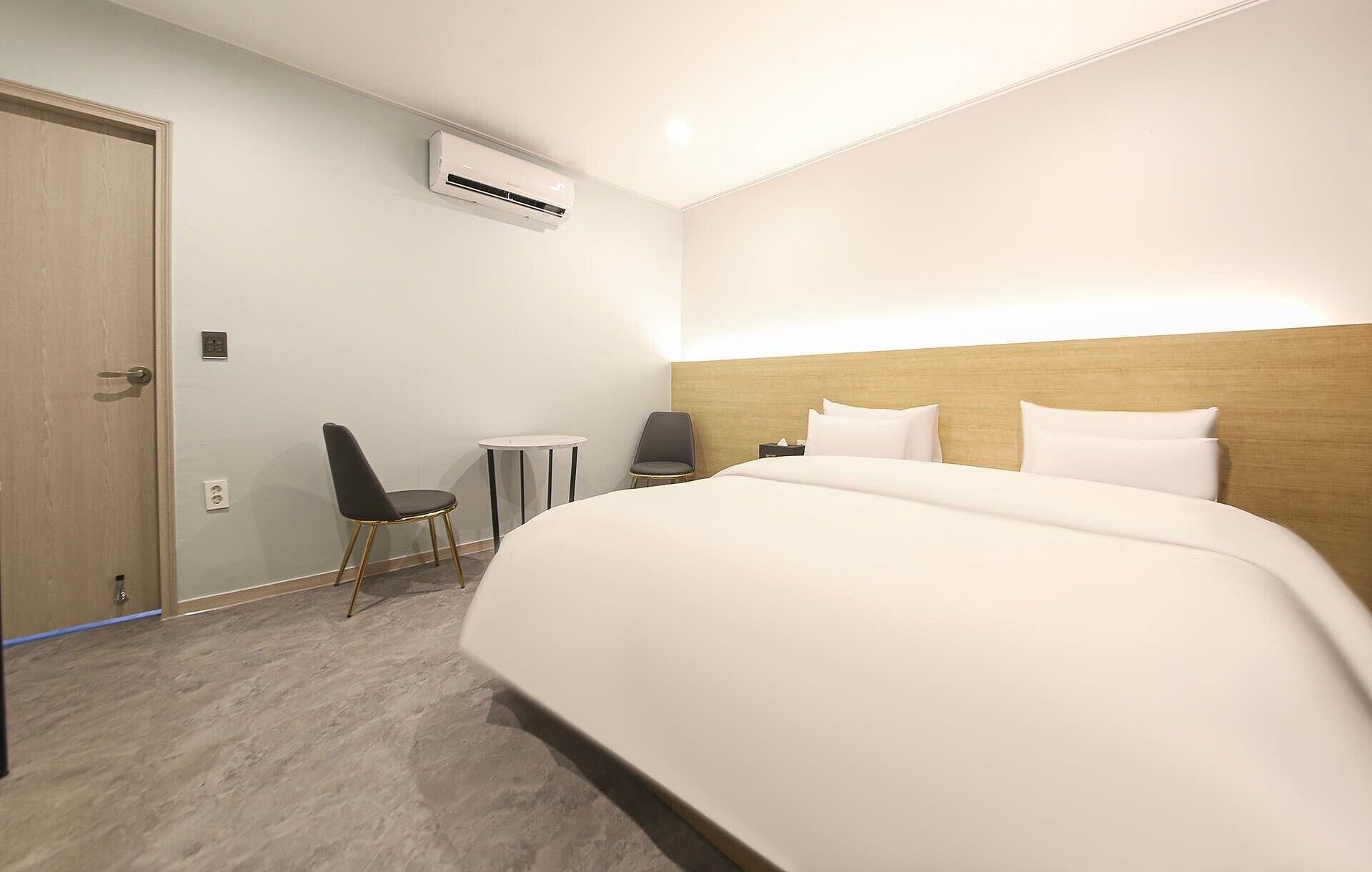 Habitación de hotel con una cama grande, una silla, una mesita y un equipo de aire acondicionado en la pared.