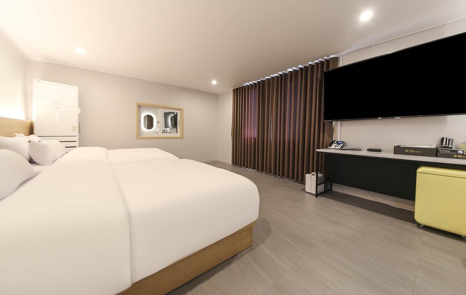 A hotel room with a large bed, a desk with a telephone, and a flat-screen TV mounted on the wall.