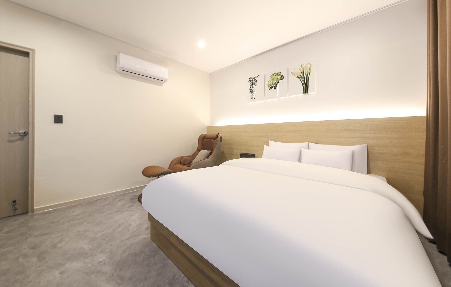 Une chambre d’hôtel dotée d’un grand lit, d’un fauteuil massant, d’un système de climatisation et d’œuvres d’art accrochées au mur.