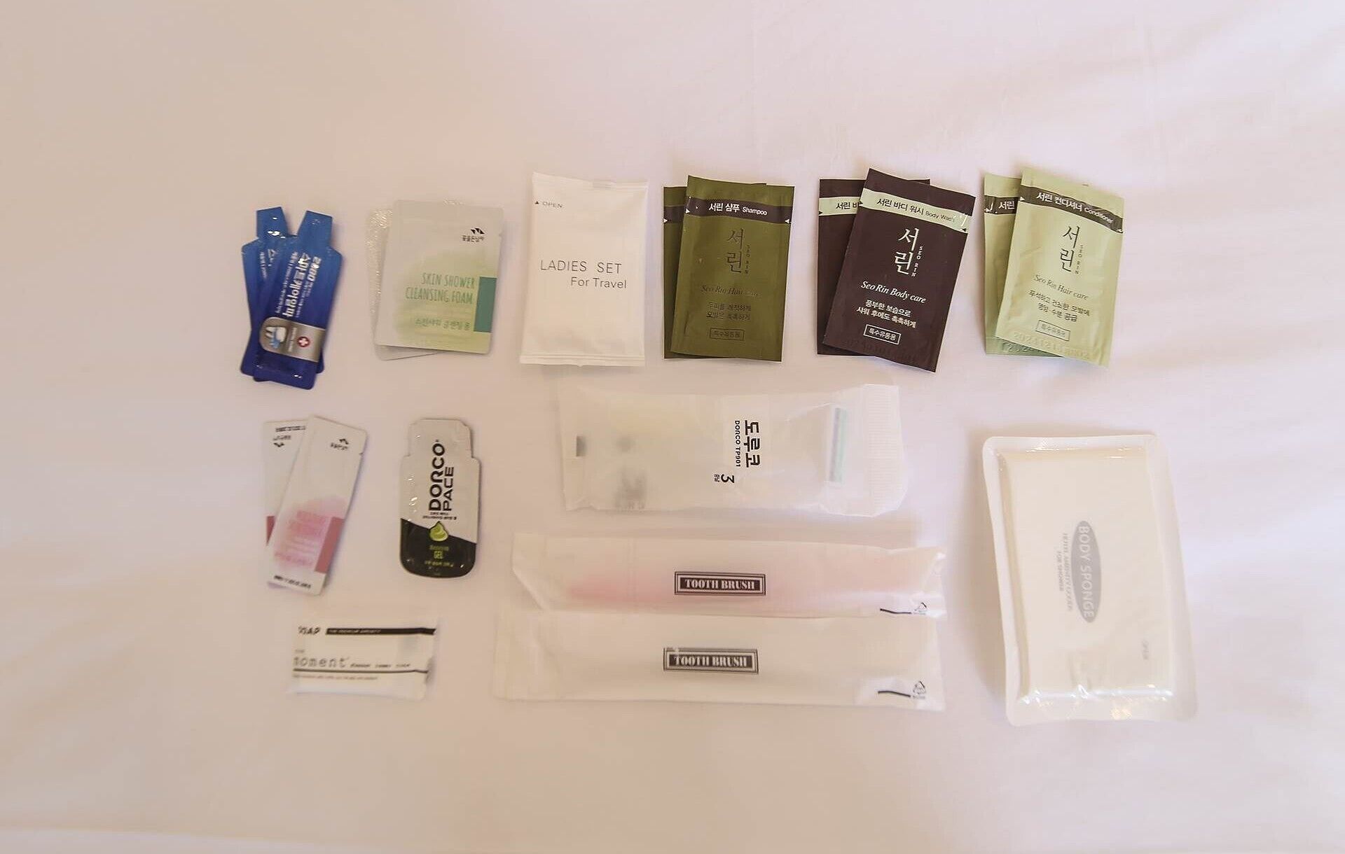 Diversos artigos de higiene pessoal dispostos sobre uma superfície branca, incluindo escova de dentes, creme dental e outros produtos de cuidado pessoal.
