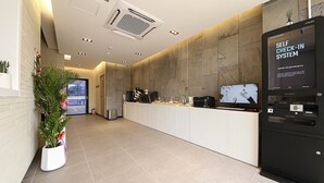 Una moderna zona de recepción con un sistema de auto-registro, un mostrador de recepción y una planta en maceta.