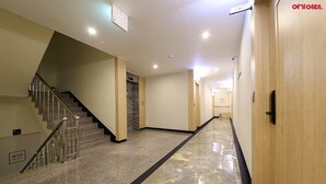 Un pasillo de hotel con suelo de mármol, una escalera a la izquierda y puertas de madera a la derecha.