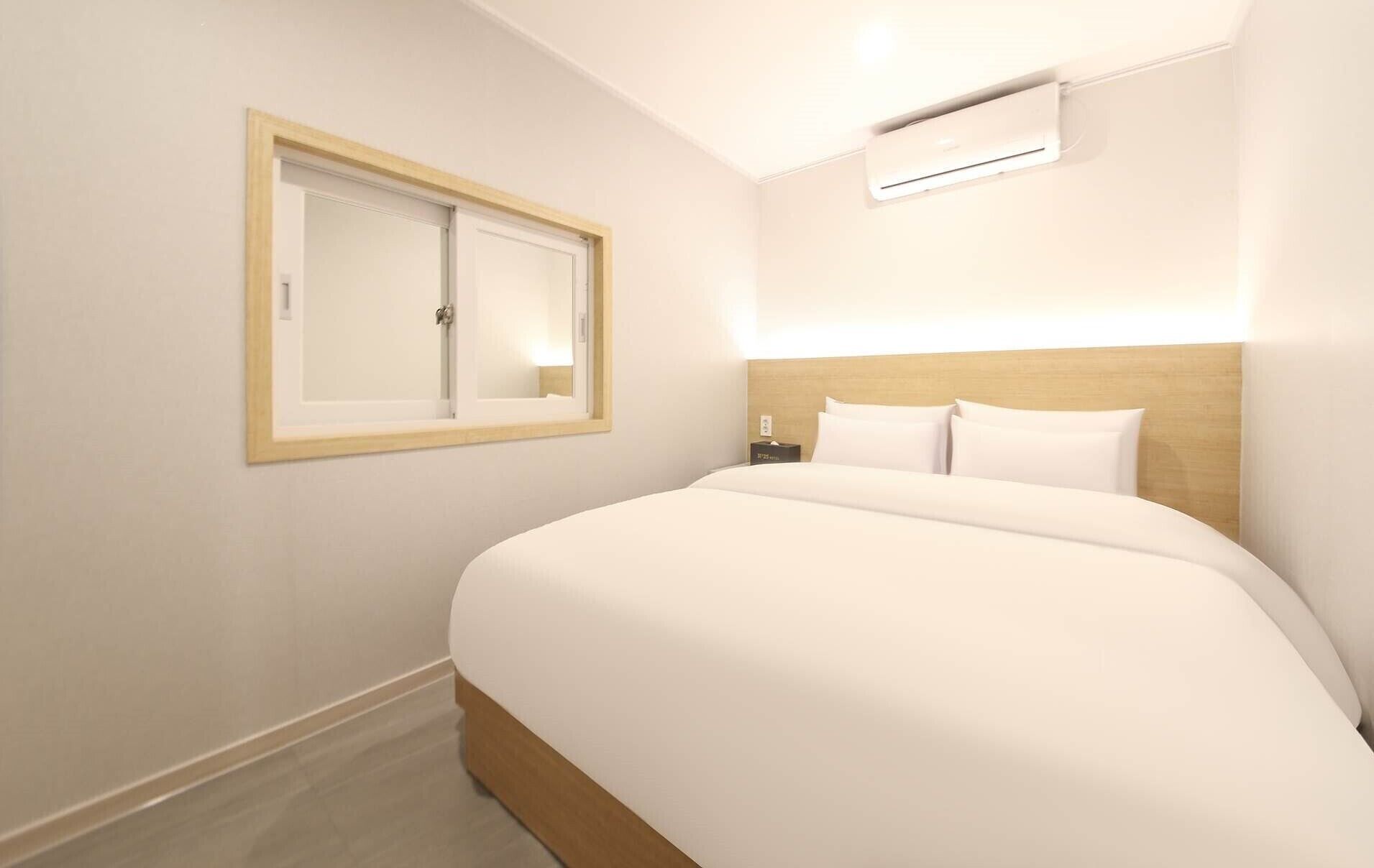 Ein Hotelzimmer mit Bett, Nachttisch, Spiegel und Klimaanlage.