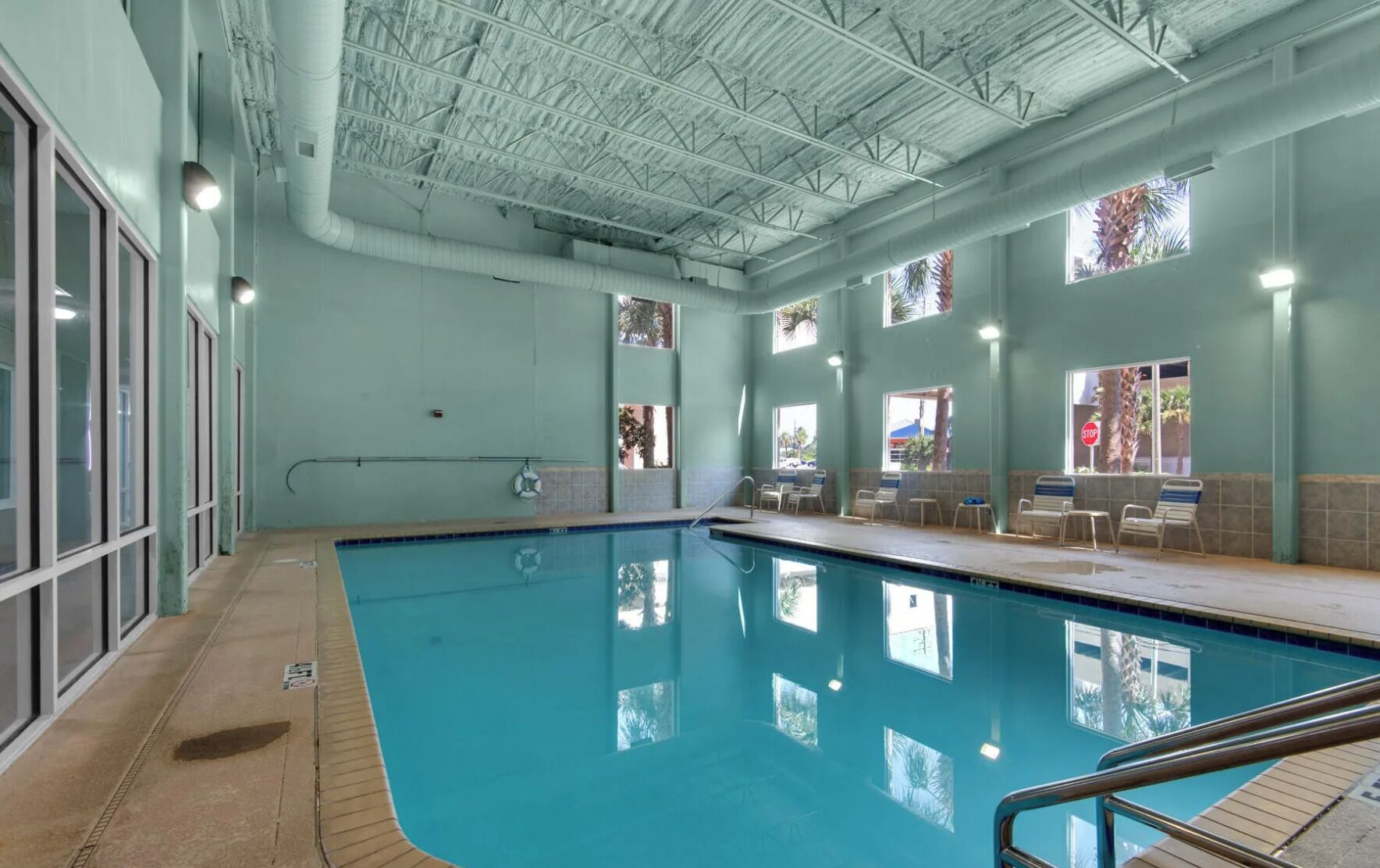 An indoor swimming pool with clear glass walls, a tiled floor, and a ceiling with visible ductwork.