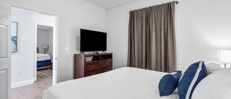 A bedroom with a large bed, a dresser, a television, and a door leading to another room.