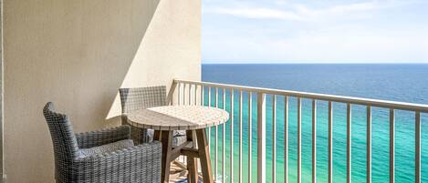 A balcony with a view of the ocean, wicker furniture, and a small round table.