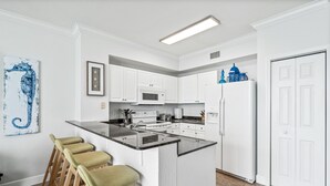 A modern kitchen with white cabinets, a central island with stools, a microwave, stove, and refrigerator. - *Aug 29 - Sept 3 Open! *Beautiful, Gulf Front!* (Panama City Beach)