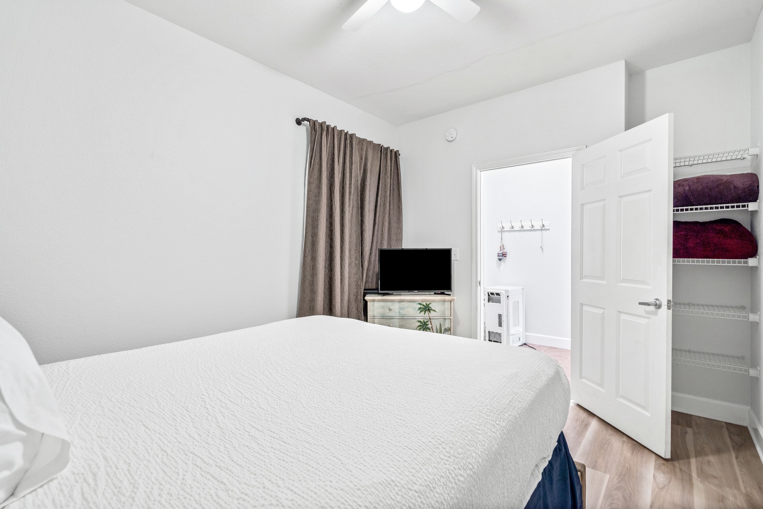 A bedroom with a bed, a TV, a dresser, a wardrobe, and a door.