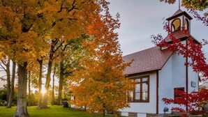 Eine weiße Kirche mit rotem Dach und Glockenturm, umgeben von Bäumen mit Herbstlaub.