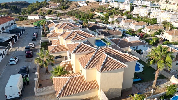 Uma área residencial costeira com edifícios de telhados em terracota, uma piscina e uma rua com carros estacionados.